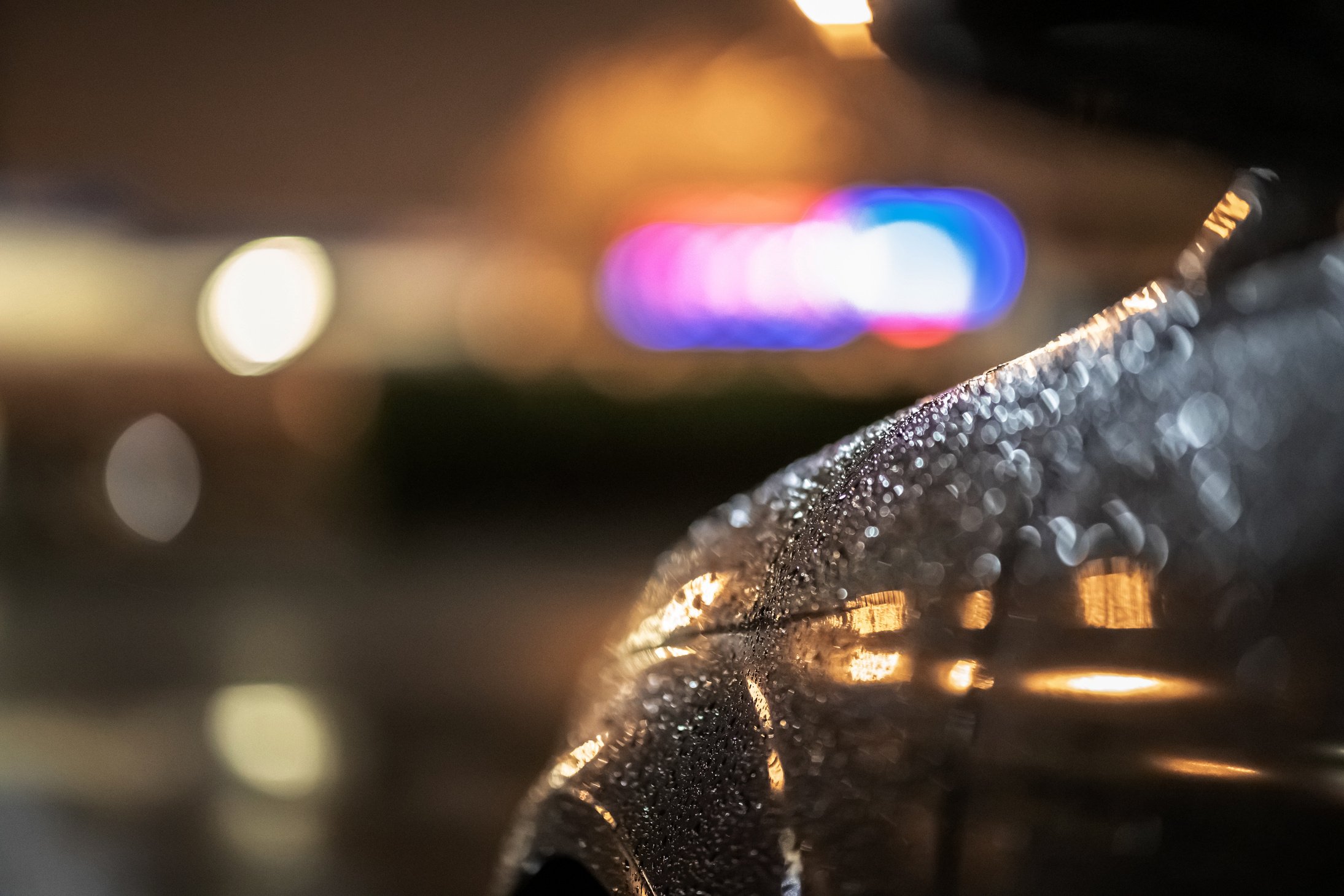 Close up of a dramatic black car at night, waiting in street lights in the heavy rain.